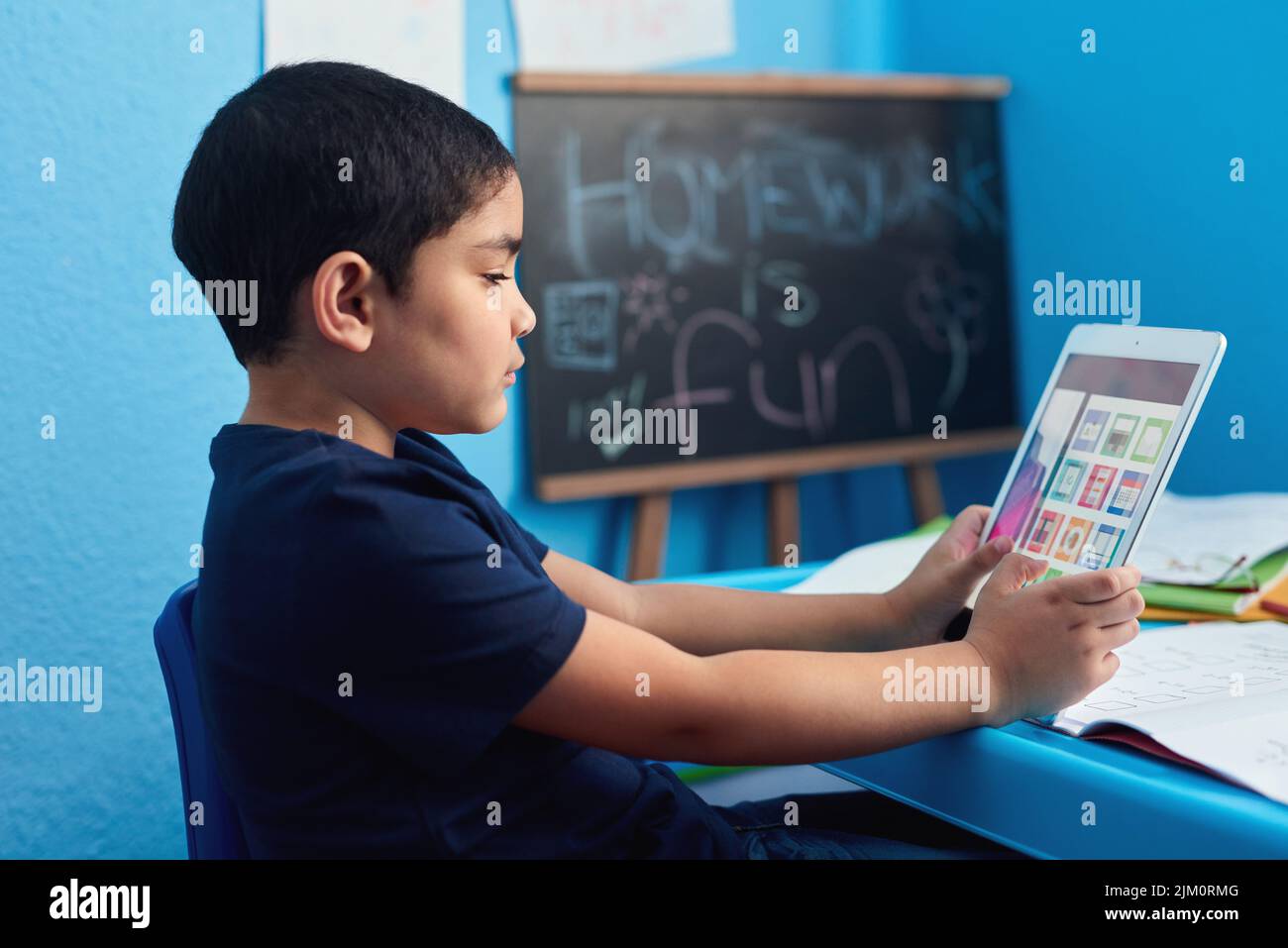 Non sostituisce un insegnante ma è piuttosto vicino. Un ragazzino adorabile che usa un tablet digitale per completare un incarico scolastico alla sua scrivania. Foto Stock