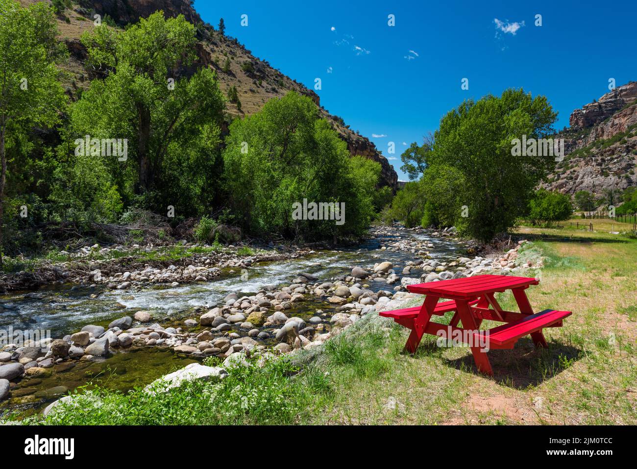 Un tavolo da picnic rosso accanto a un ruscello circondato dal verde Foto Stock