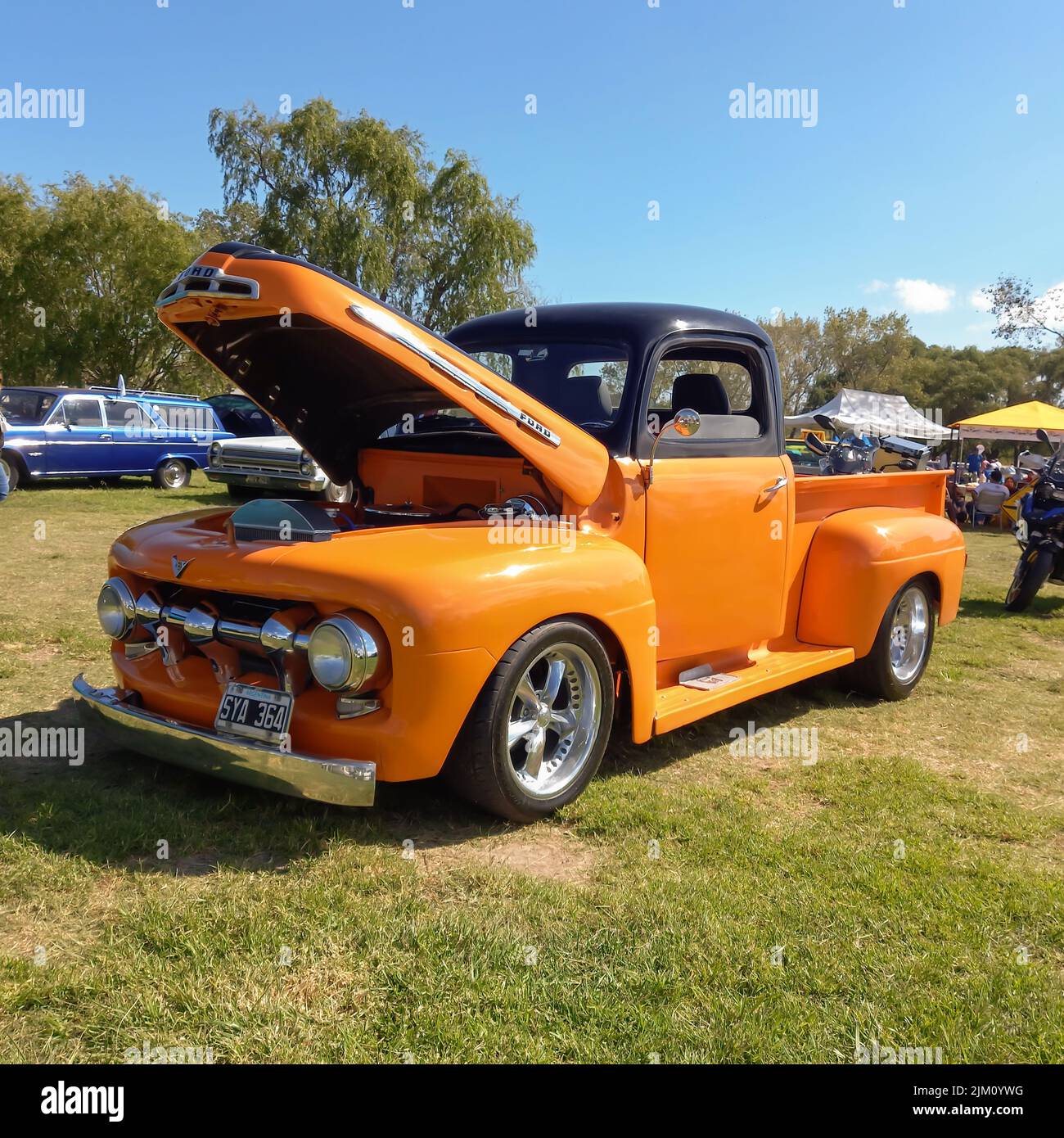 Chascomus, Argentina - Apr 09, 2022: Vecchio camion arancione di servizio pick-up Ford F 1 1950s in campagna. Aprire il cofano. Erba naturale e alberi. Auto classica Foto Stock