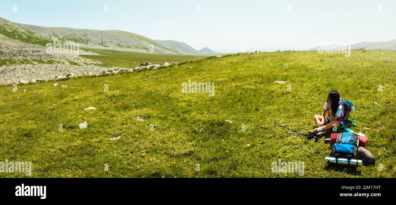 Giovane donna caucasica escursionista sedersi in montagna da solo chiamare i genitori emergenza con smartphone in destinazione remota all'aperto in vacanza coppia Foto Stock