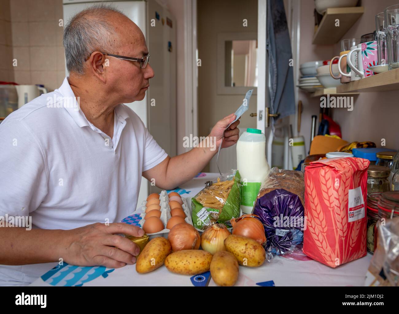 Un uomo anziano in cucina che controlla il costo del cibo essenziale quotidiano, in quanto l'aumento dell'inflazione e il costo della vita influenzano il tenore di vita. Foto Stock