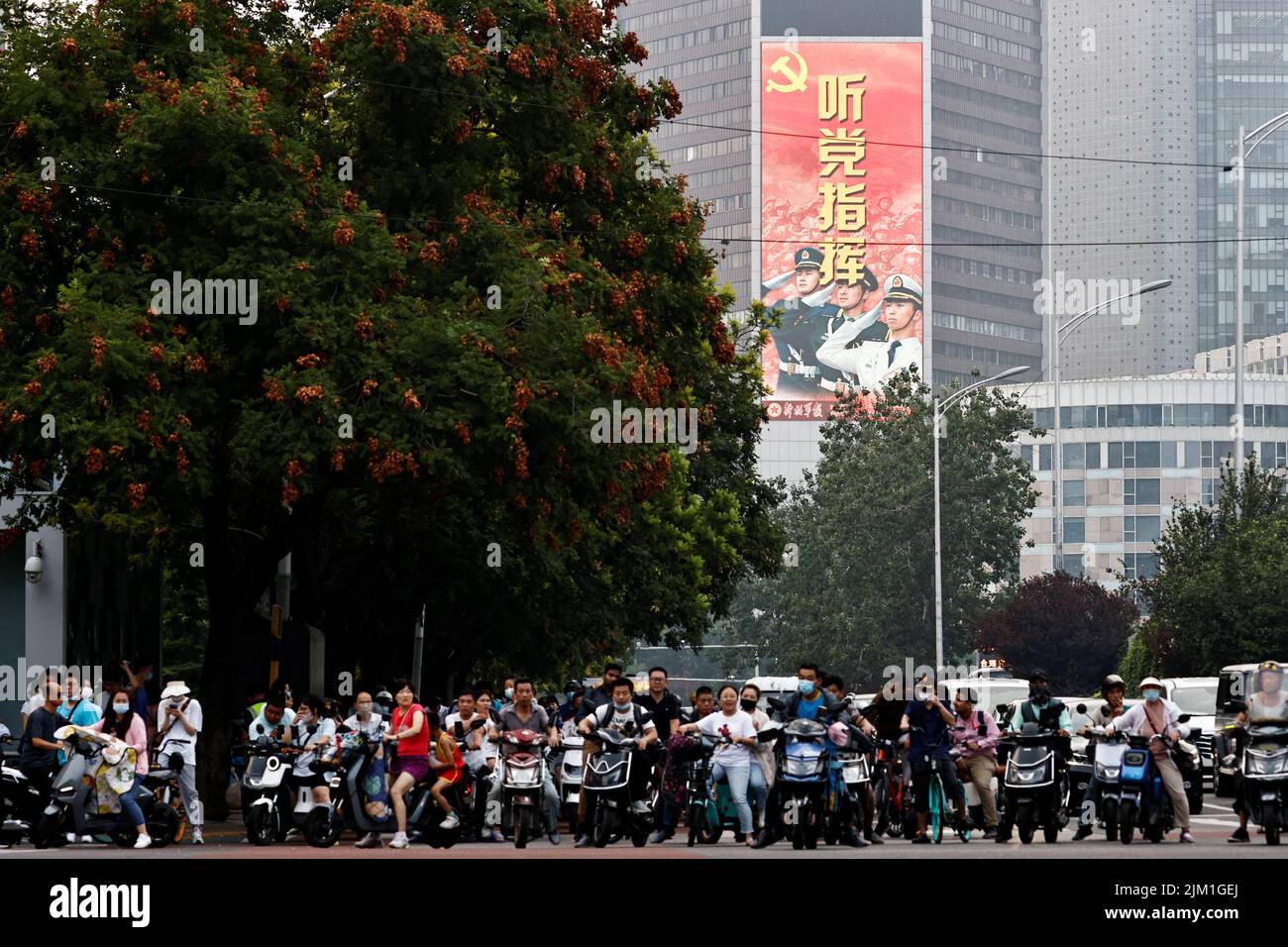 Le persone che guidano veicoli aspettano un incrocio vicino a uno schermo che mostra un'immagine dell'Esercito popolare Cinese di Liberazione (PLA) a Pechino, Cina 4 agosto 2022. REUTERS/Thomas Peter Foto Stock