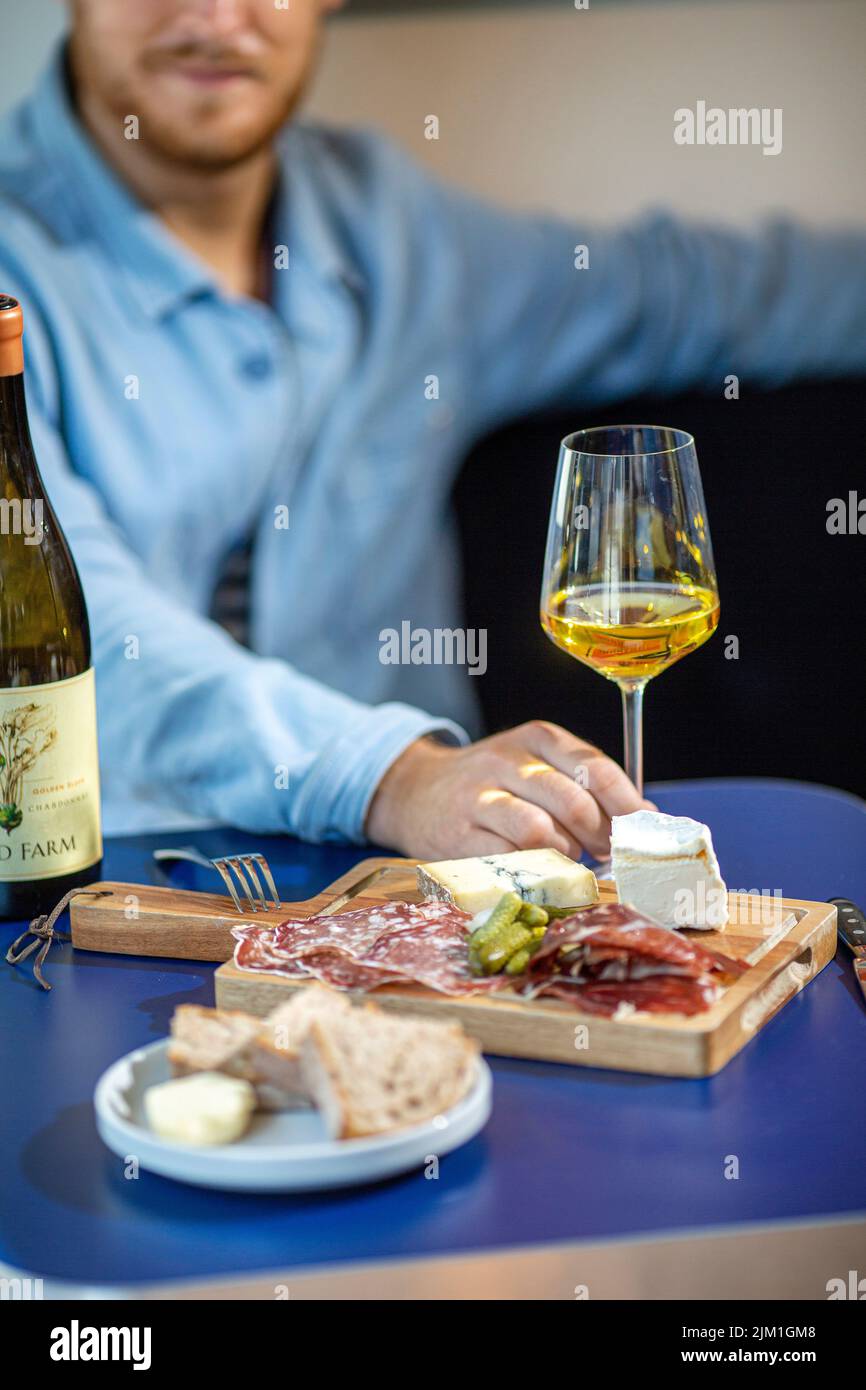 maschio con bicchiere di vino bianco, salumi e cartone di formaggio. Foto Stock