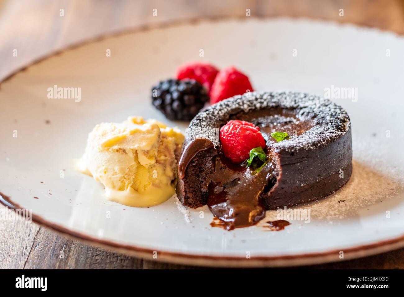 Fondente al cioccolato (cupcake) con lamponi, gelato e zucchero in polvere posto sul piatto Foto Stock