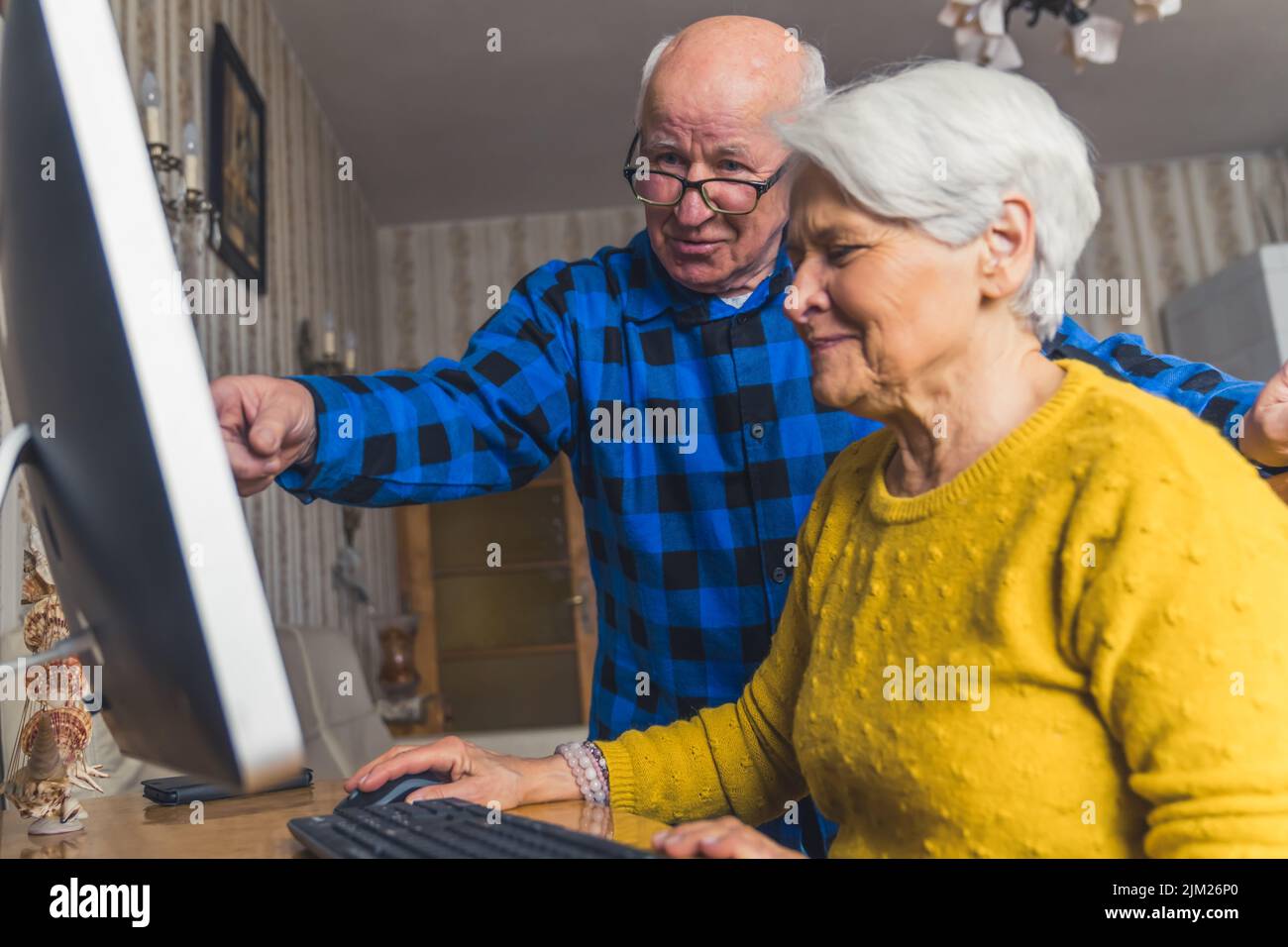 Uomo anziano con esperienza moderna che punta al monitor e spiega a sua moglie come usare il computer . Foto di alta qualità Foto Stock