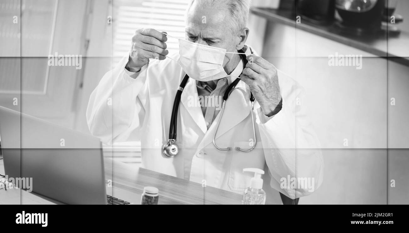 Medico senior che mette su una maschera medica in ufficio medico, modello geometrico Foto Stock
