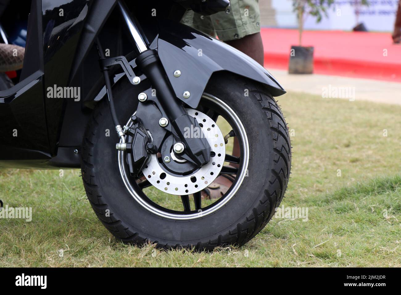 Ruota anteriore di uno scooter elettrico parcheggiato su un prato con vista delle sospensioni e delle rotture del disco Foto Stock