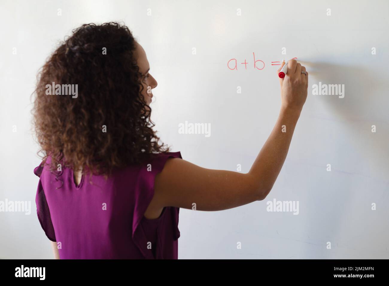 Giovane insegnante caucasica che scrive formula sulla lavagna durante la lezione di matematica a scuola Foto Stock