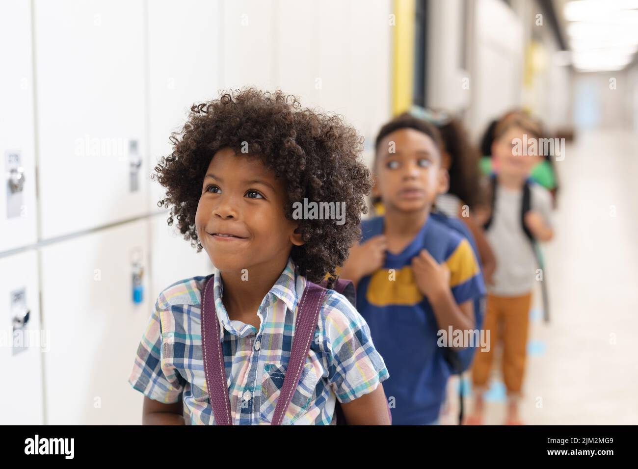 Bambini multirazziali innocenti della scuola elementare in fila da armadietti Foto Stock