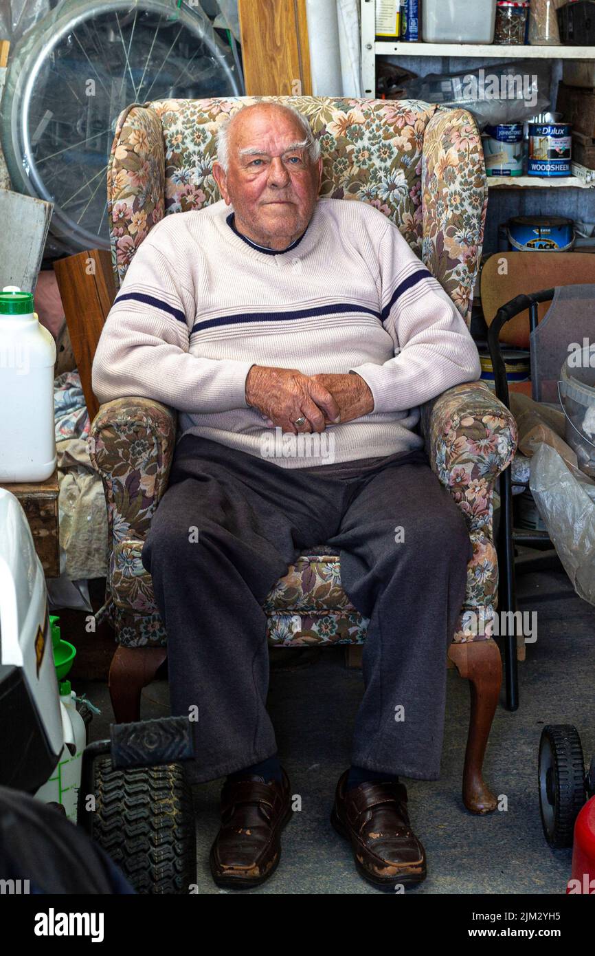 Uomo anziano seduto in una vecchia poltrona nel suo capannone Foto Stock