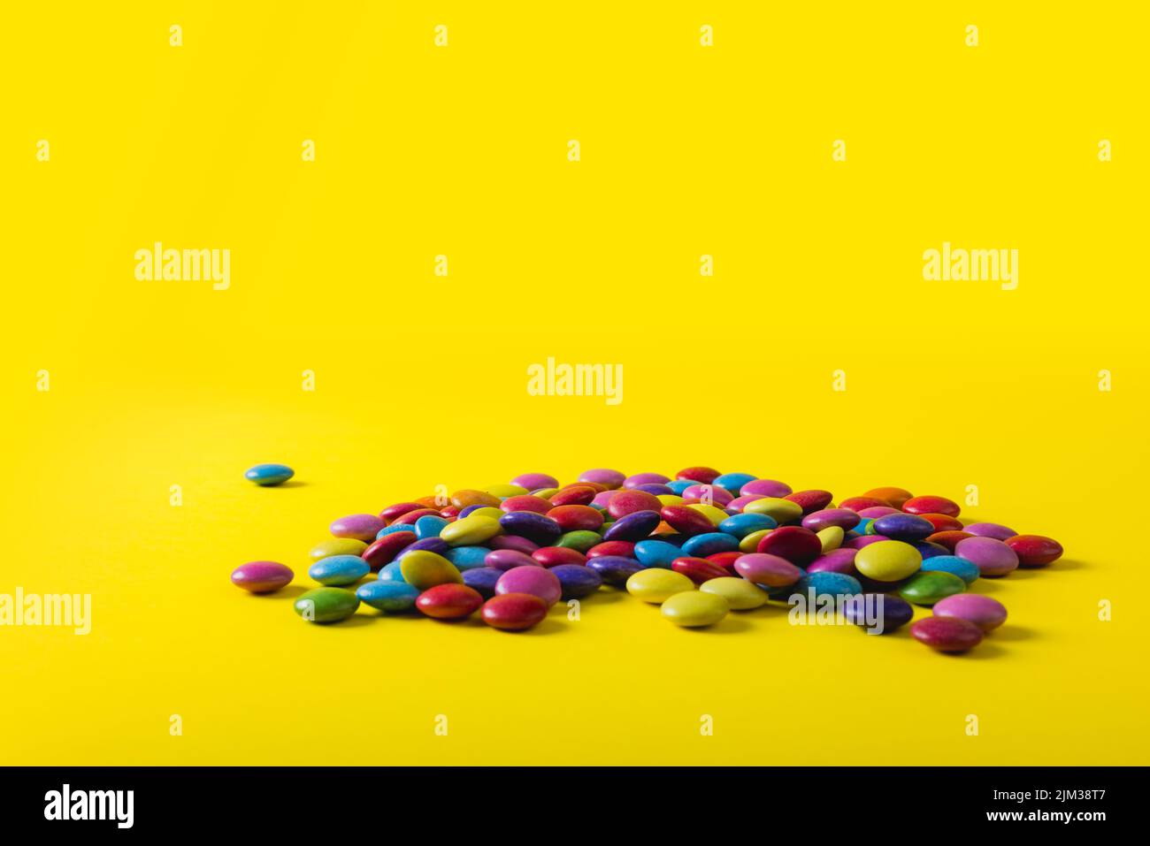 Pila di caramelle al cioccolato multicolore con spazio copia su sfondo giallo Foto Stock