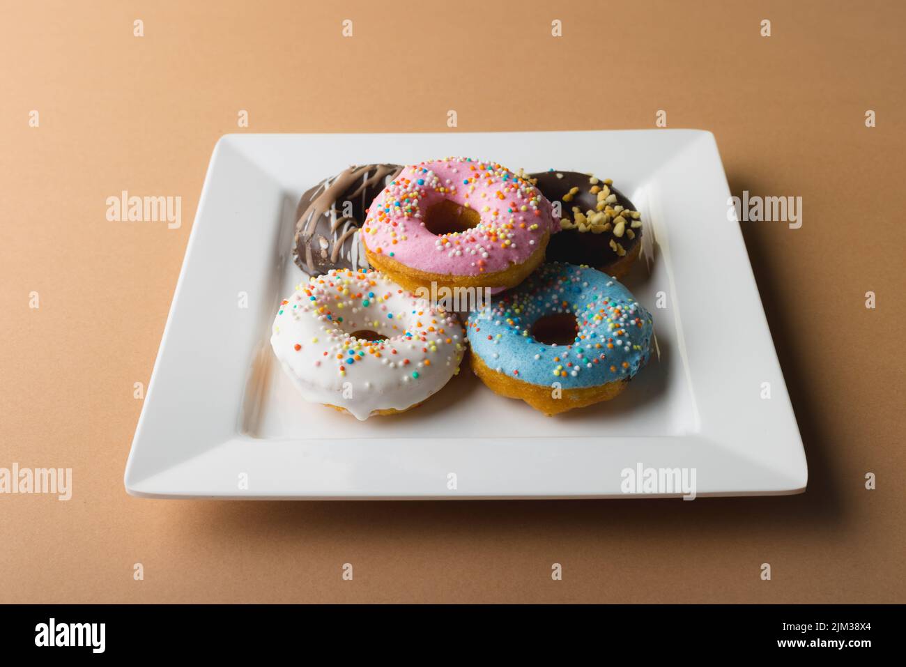 Vista ad angolo alto di ciambelle fresche in piatto bianco su sfondo beige Foto Stock