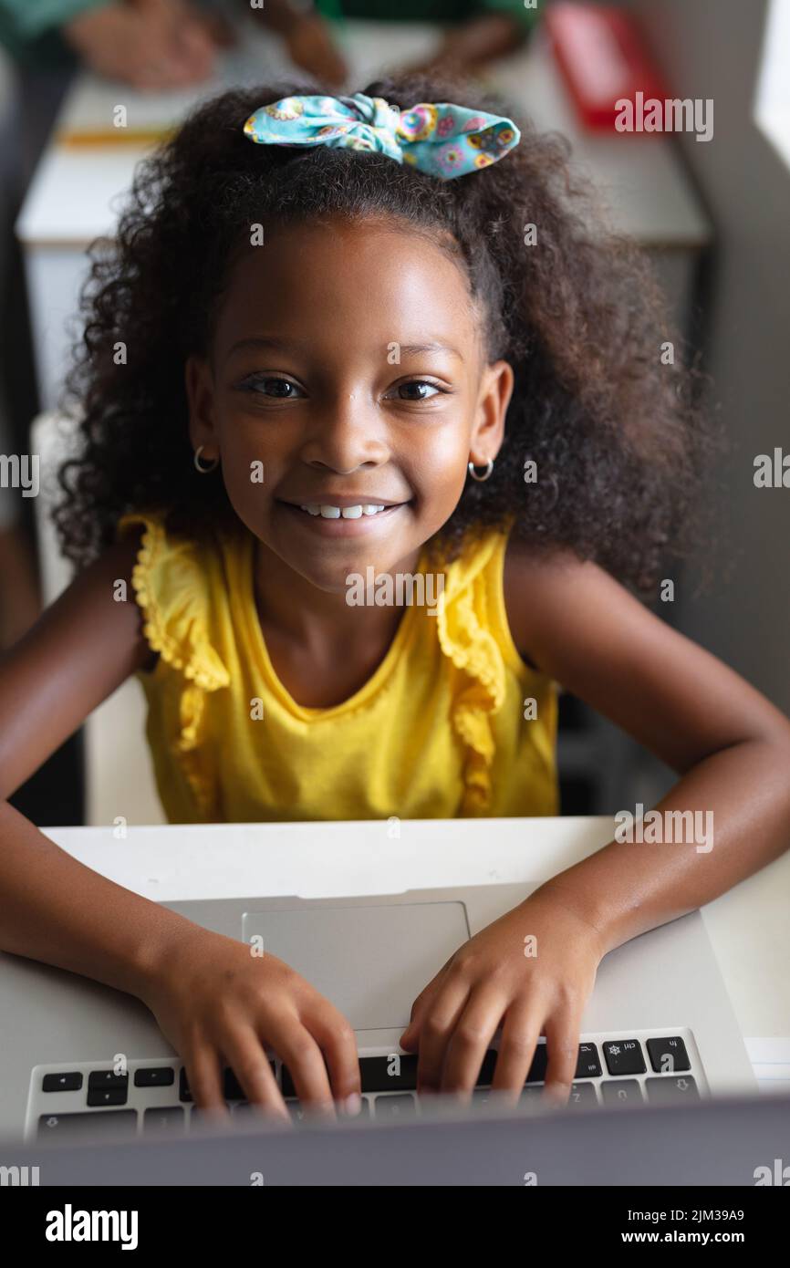 Ritratto di sorridente studentessa elementare afroamericana che utilizza un computer portatile alla scrivania in classe computer Foto Stock