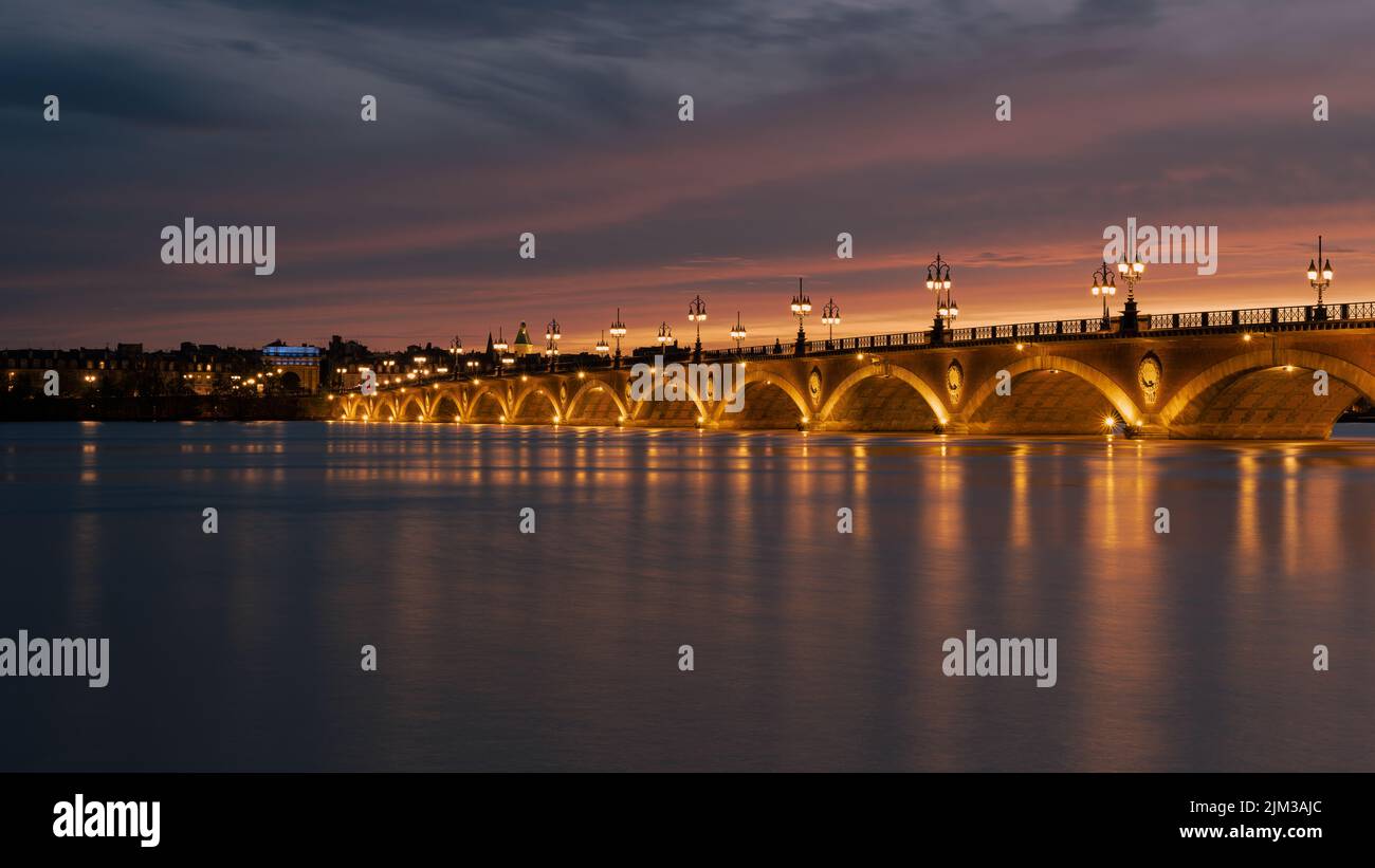 Pont de Pierre che attraversa il fiume Garonna nella città di Bordeaux illuminato al tramonto con la Basilique Saint-Michel sullo sfondo Foto Stock