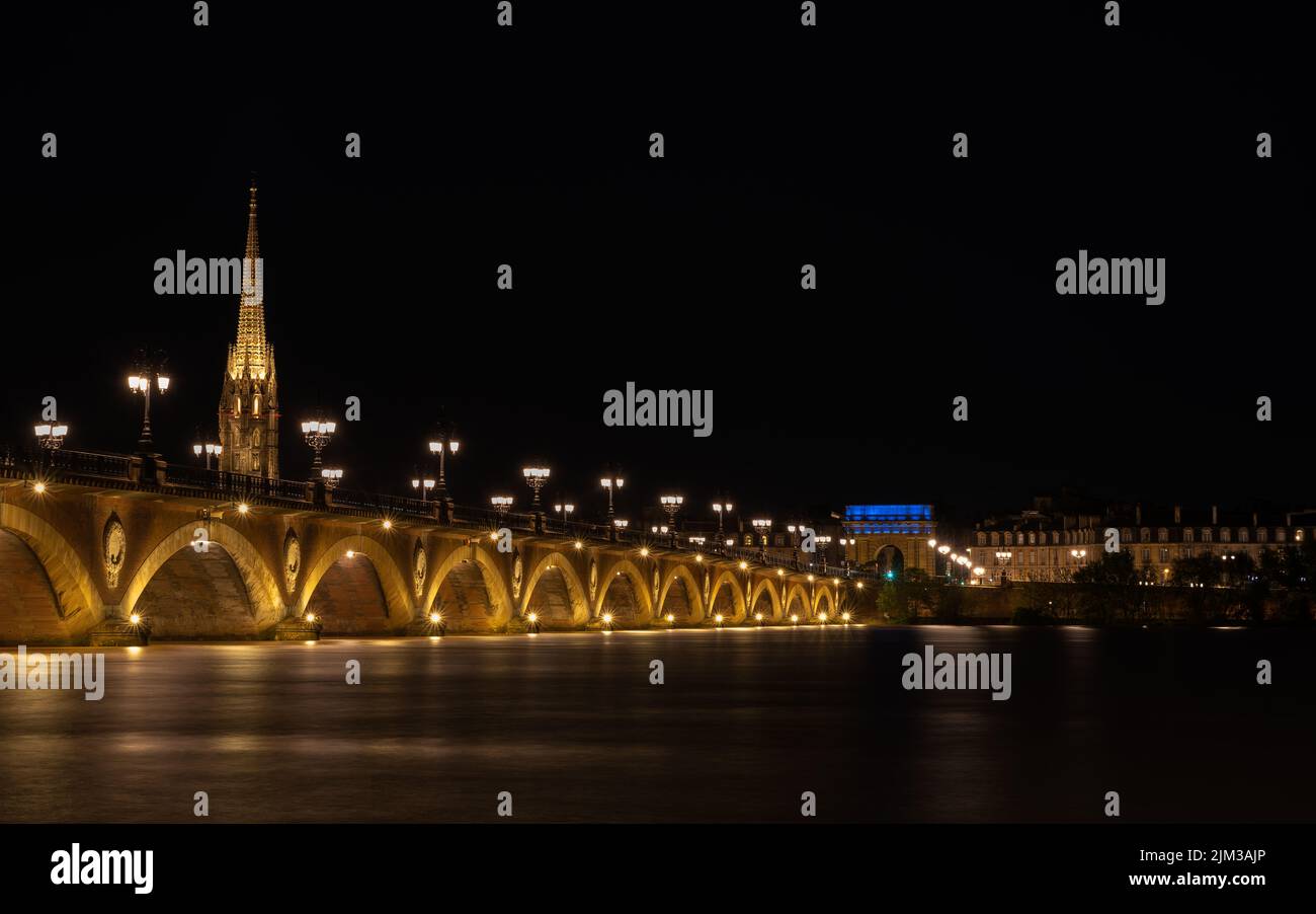Pont de Pierre che attraversa il fiume Garonna nella città di Bordeaux illuminata di notte con la Basilique Saint-Michel sullo sfondo Foto Stock