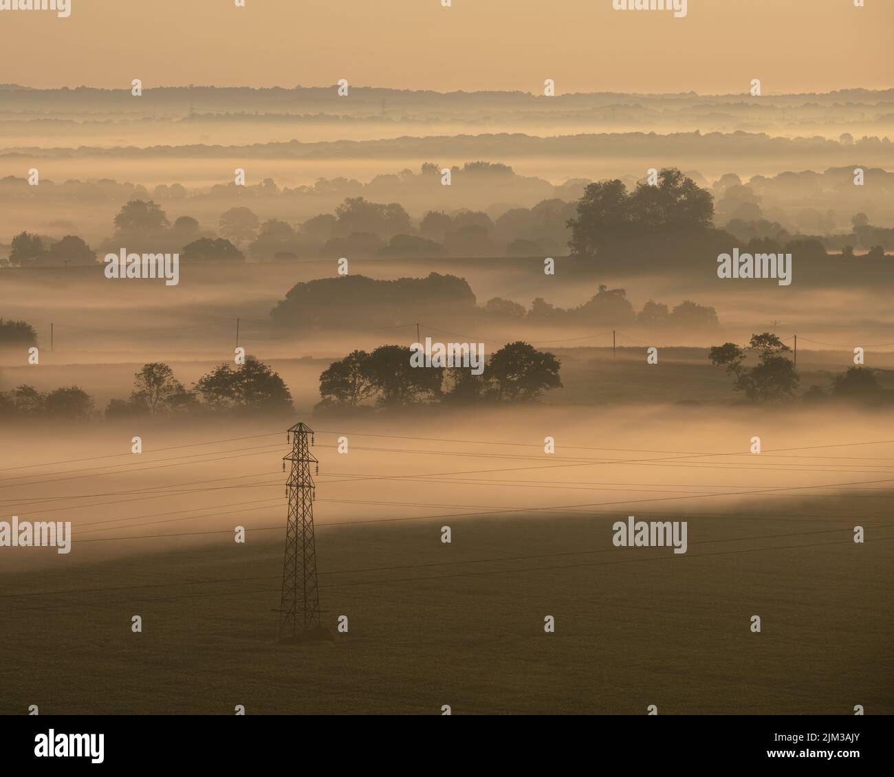 Un traliccio di elettricità si erge da solo quando la nebbia mattutina copre il paesaggio del Sussex orientale vicino a Lewes. Foto Stock