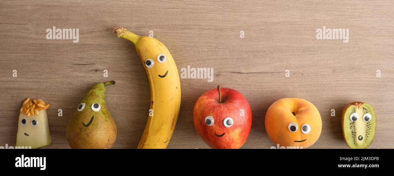 Fila di frutta divertente con occhi e bocche come concetto per motivare i bambini a mangiare. Vista dall'alto. Foto Stock