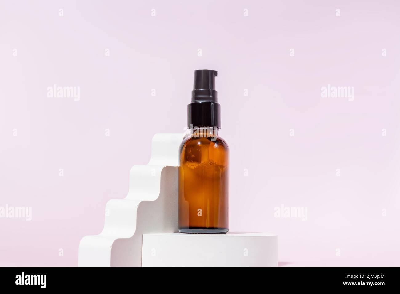 Bottiglia in vetro ambrato con coperchio nero su un podio su sfondo rosa chiaro. Prodotti per la cura della pelle, cosmetici naturali. Concetto di bellezza per viso e corpo ca Foto Stock