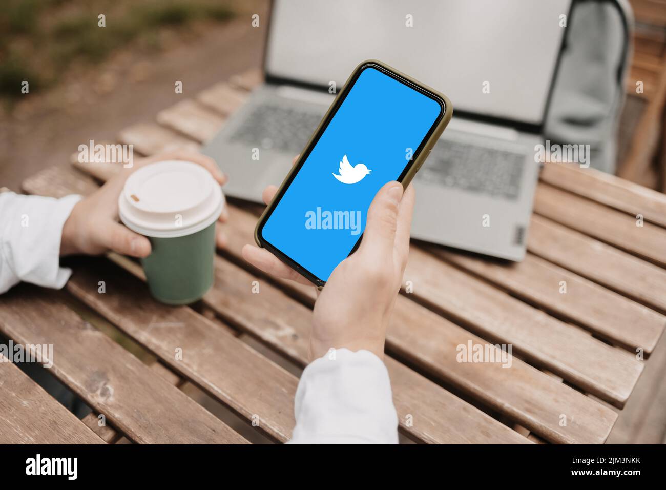 Una mano con il caffè e un telefono con Twitter social network Foto Stock