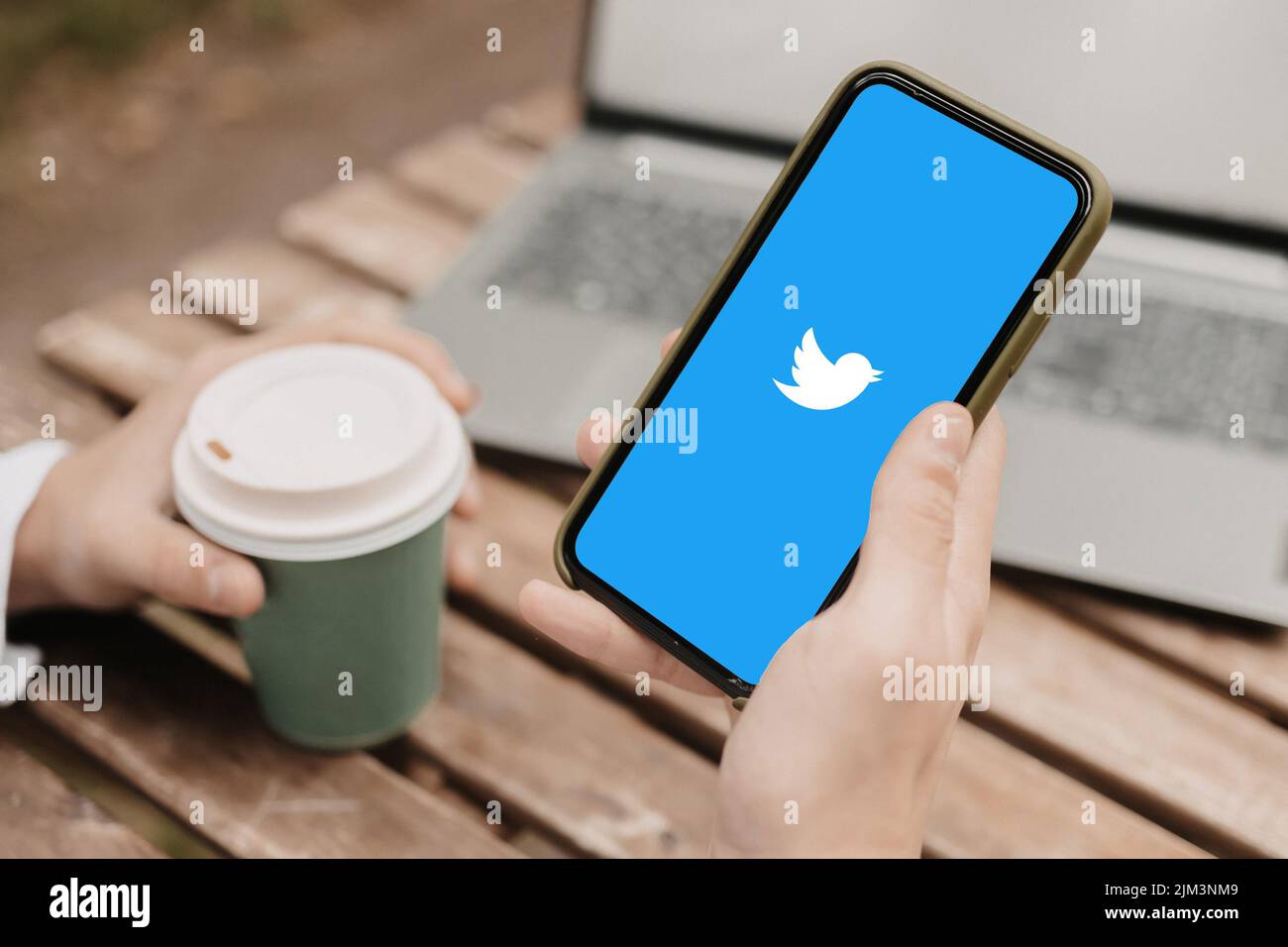Una mano con il caffè e il telefono, visitando l'app Twitter sul telefono Foto Stock