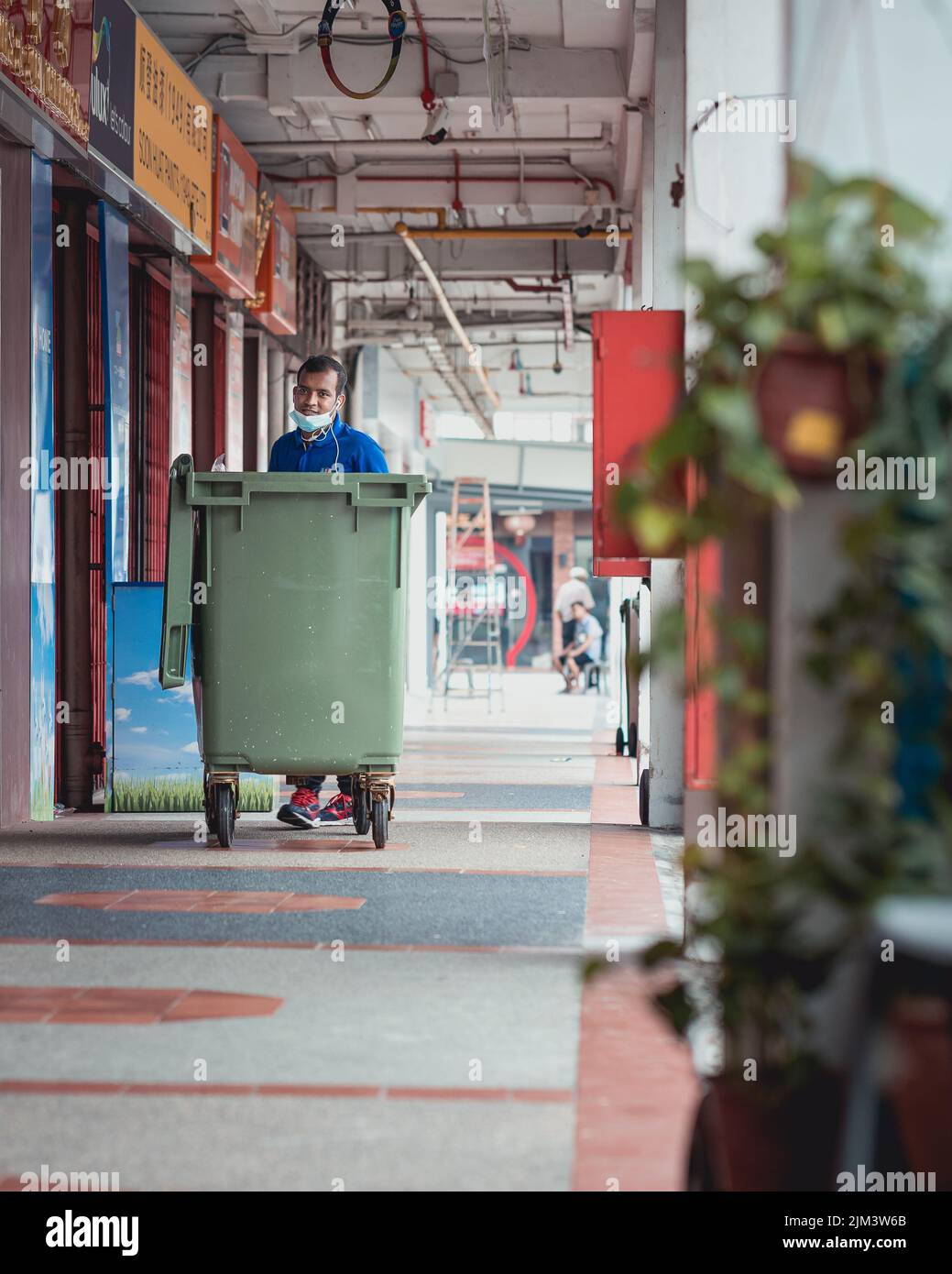 Un colpo verticale di un lavoratore che spinge un bidone di raccolta rifiuti lungo il corridoio di Singapore Foto Stock