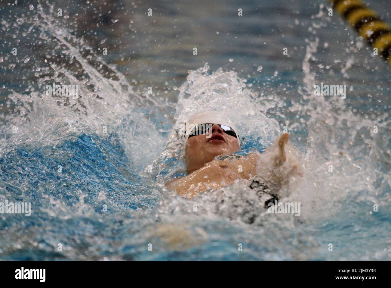 Primo piano di un nuotatore maschile che fa il backstoke in una piscina. Foto Stock
