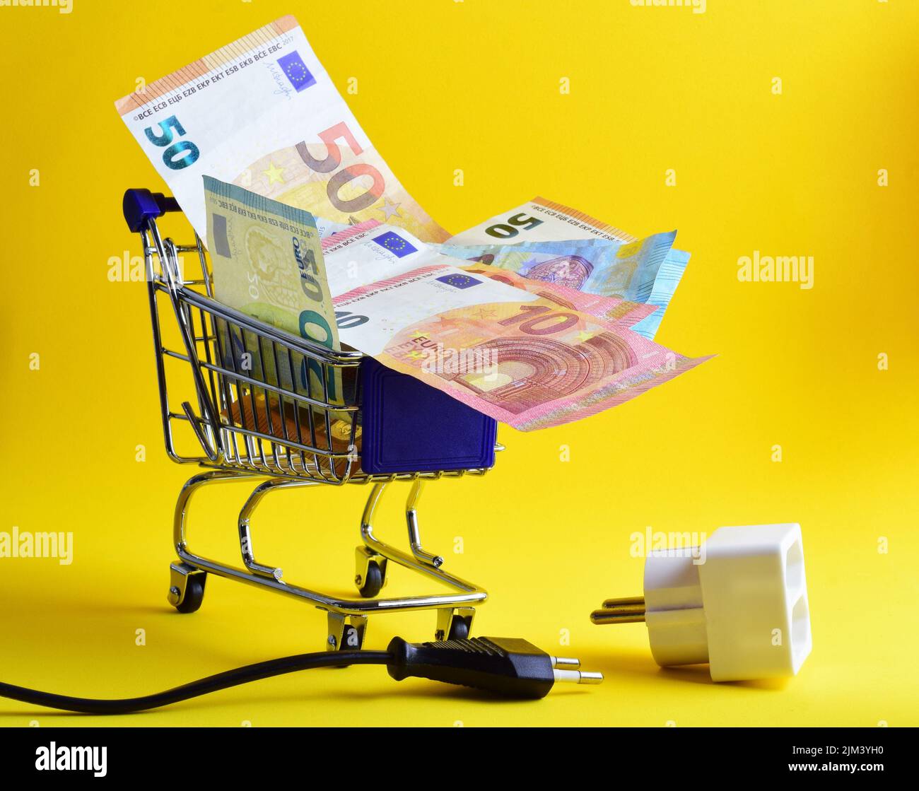 Un carrello con banconote in euro e una presa isolata su sfondo giallo.aumento dei prezzi in energia Foto Stock