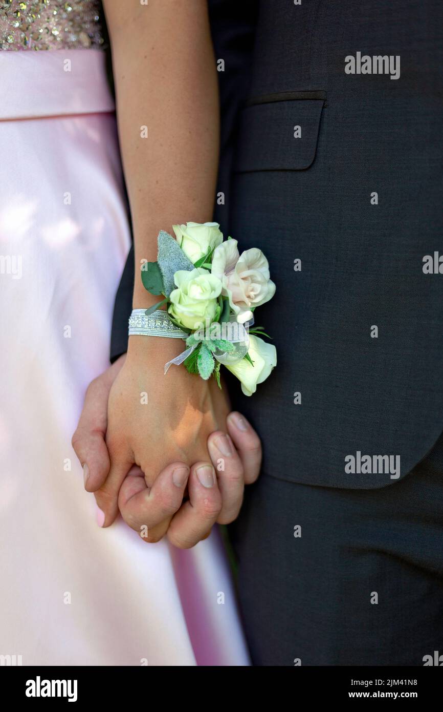 Un primo piano di una giovane coppia che tiene le mani con un corsago da polso di fiore al loro promo con sfondo sfocato Foto Stock