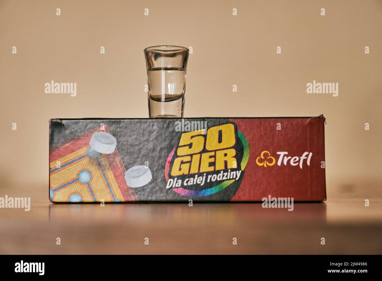 Un bicchiere di vodka su una scatola di marca Trefl con cinquanta giochi su un tavolo lucido Foto Stock