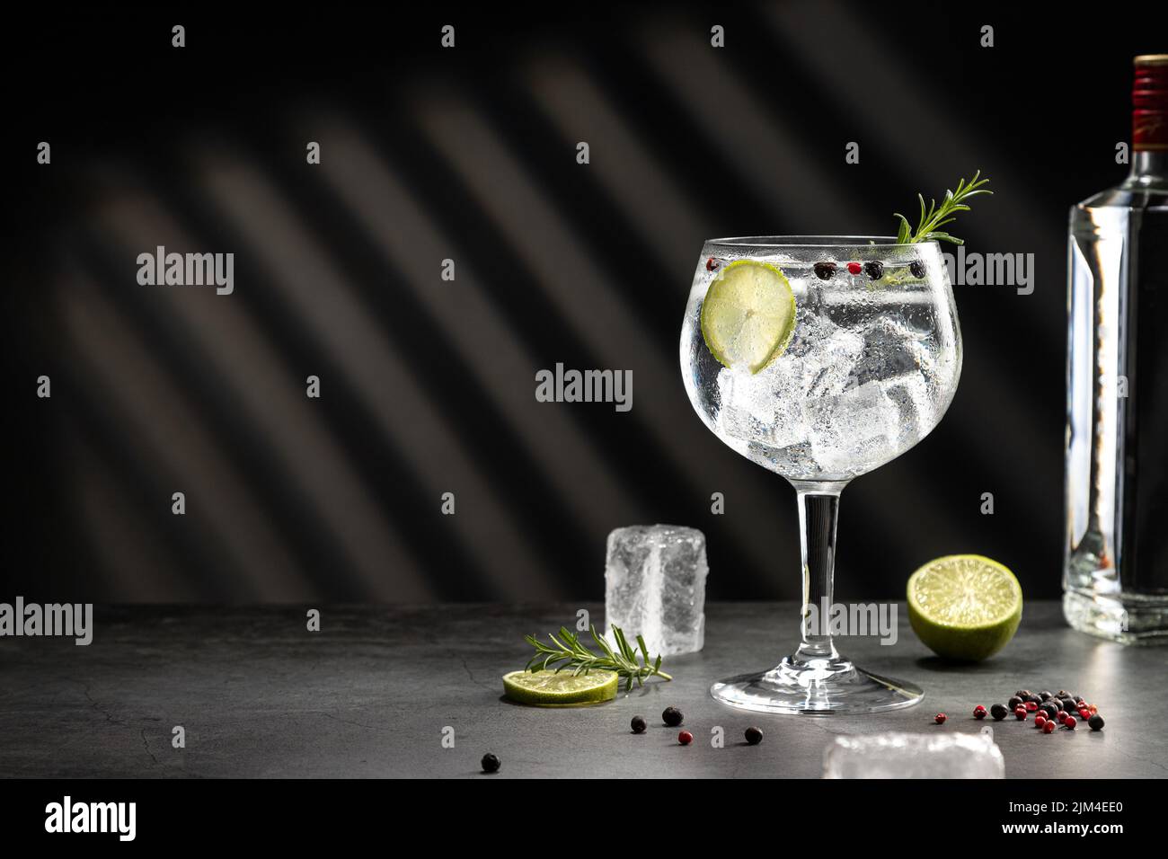 Vetro freddo di gin tonico con ghiaccio e ombre dure su sfondo grigio scuro con spazio di copia. Foto Stock
