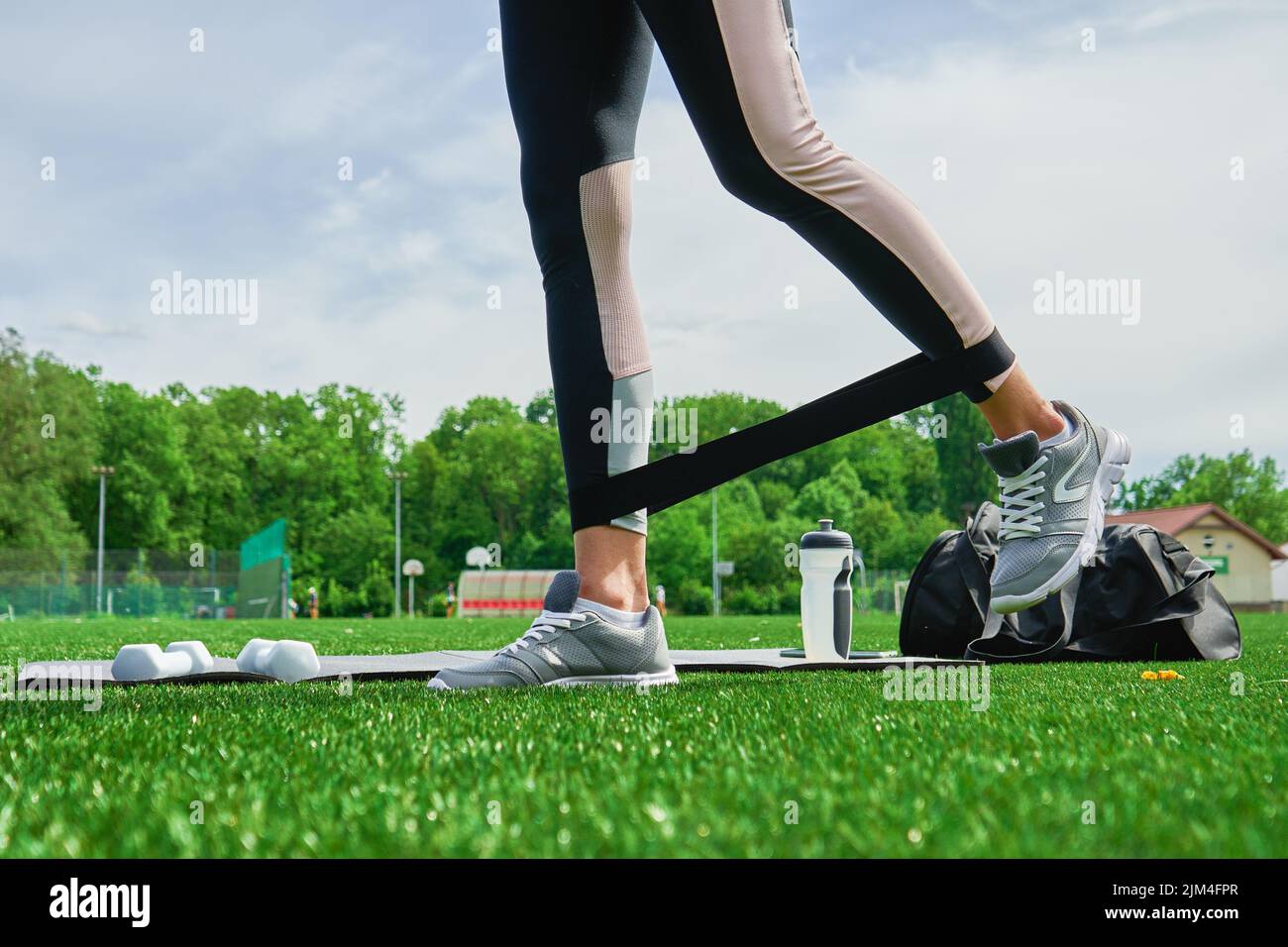 Le gambe femminili fanno l'esercitazione di workout con la fascia matura elastica all'erba verde, l'addestramento della donna di sport all'aperto, il fitness per concetto sano di lifestyle Foto Stock