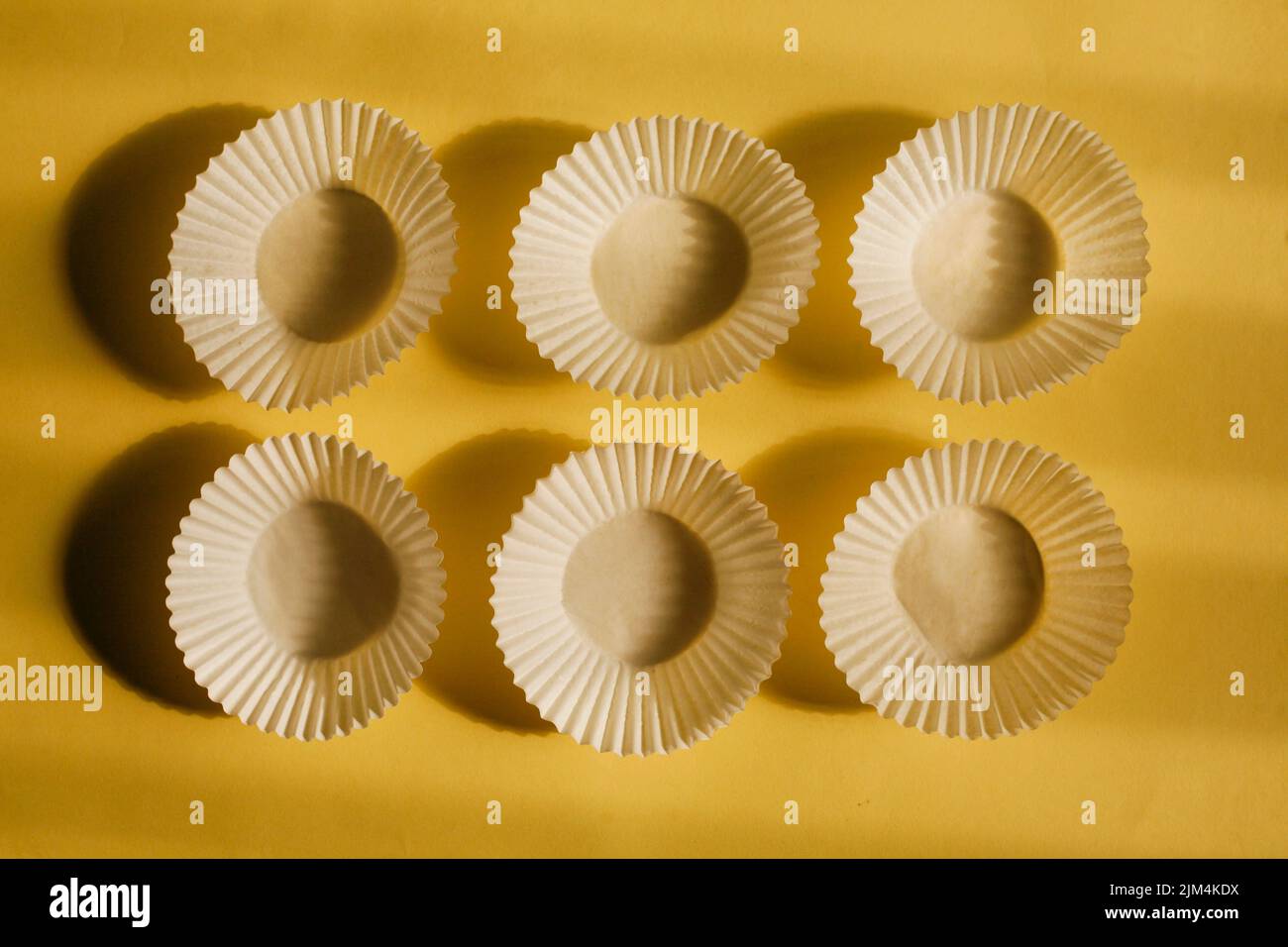 tazzine vuote di carta da forno. tazzine bianche di carta da biscotto isolate su sfondo giallo con ombra Foto Stock
