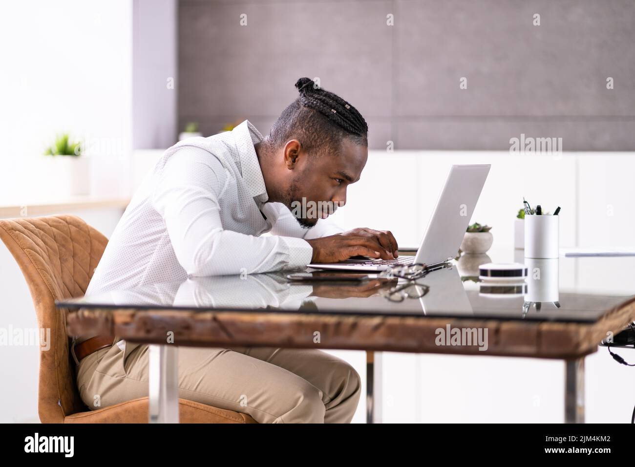 Uomo africano cattiva postura di lavoro digitando alla scrivania Foto Stock