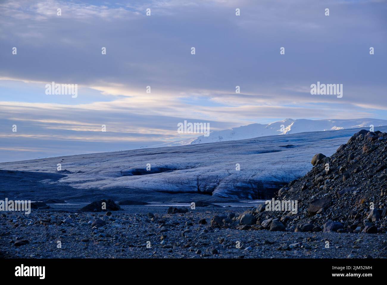 Il bordo sottile di un ghiacciaio mentre è spinto giù la valle. Moraine in primo piano e montagne innevate sullo sfondo Foto Stock