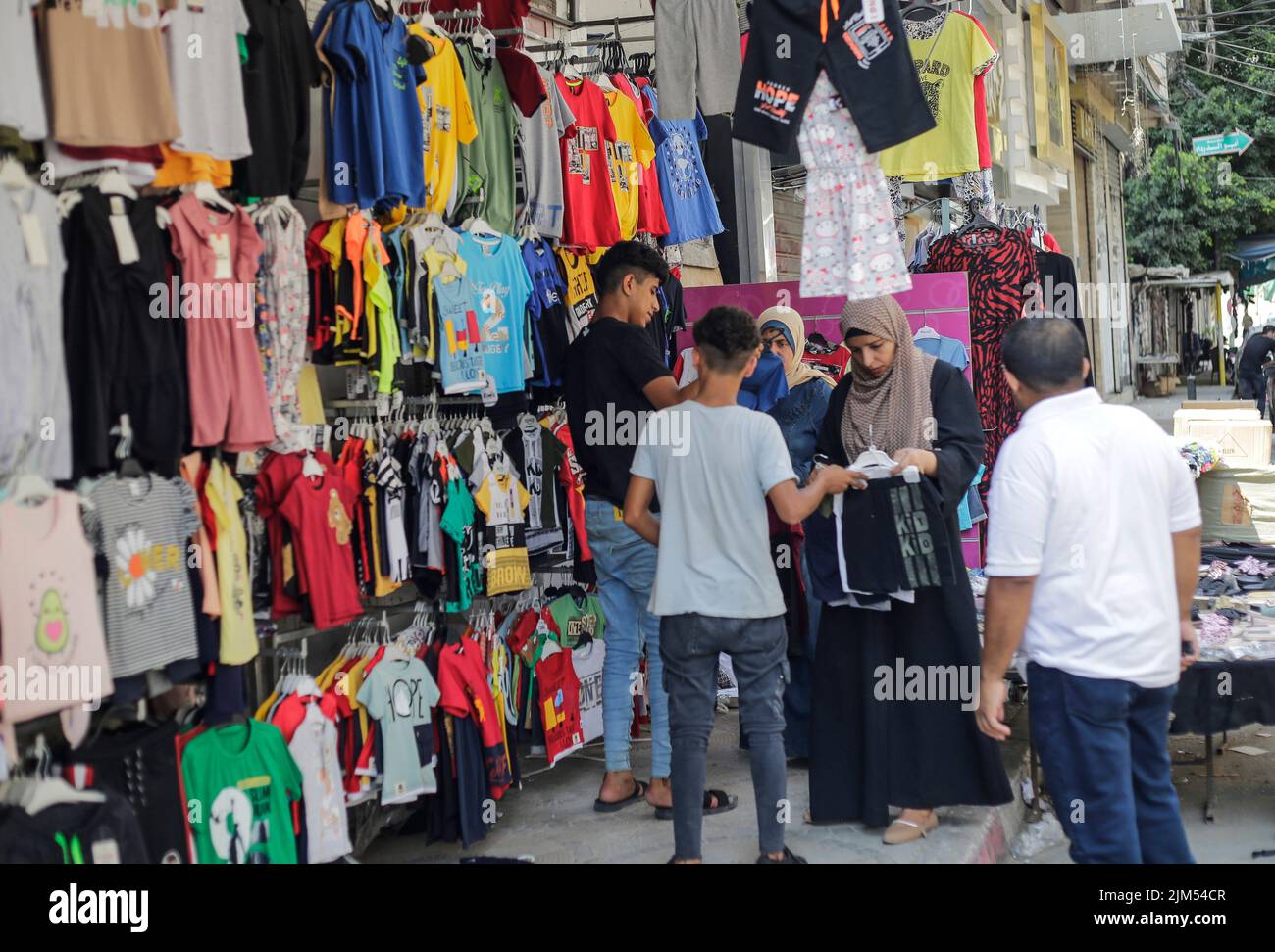 I palestinesi hanno visto fare shopping in un negozio di abbigliamento a Gaza. I leader di Hamas a Gaza hanno imposto un mucchio di nuove tasse sulle importazioni di abbigliamento e forniture per ufficio prima del nuovo anno scolastico, scatenando proteste limitate ma rare nell'impoverita enclave costiera. Arriva in un momento in cui 2,3 milioni di persone a Gaza soffrono del blocco israeliano di 15 anni, ma anche di un nuovo salto di prezzi causato dai problemi della catena di approvvigionamento globale e dall'invasione russa dell'Ucraina. La lista del Ministero dell'Economia include le tasse pianificate su articoli come noci imballate, con una tariffa d'importazione di 2.000 shekel (circa $600) Foto Stock