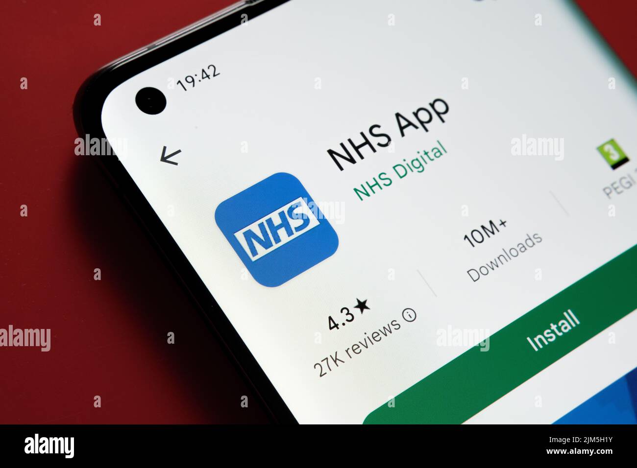 App NHS visualizzata in Google Play Store sullo schermo dello smartphone su sfondo rosso. Foto ravvicinata con messa a fuoco selettiva. Stafford, Regno Unito, Au Foto Stock