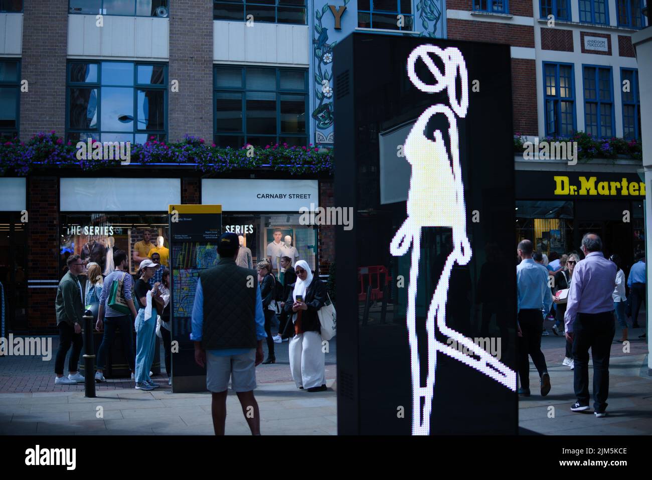 Una donna segno sullo schermo pubblicitario pubblico con le persone in fondo alla strada, Soho Walk a Londra Foto Stock