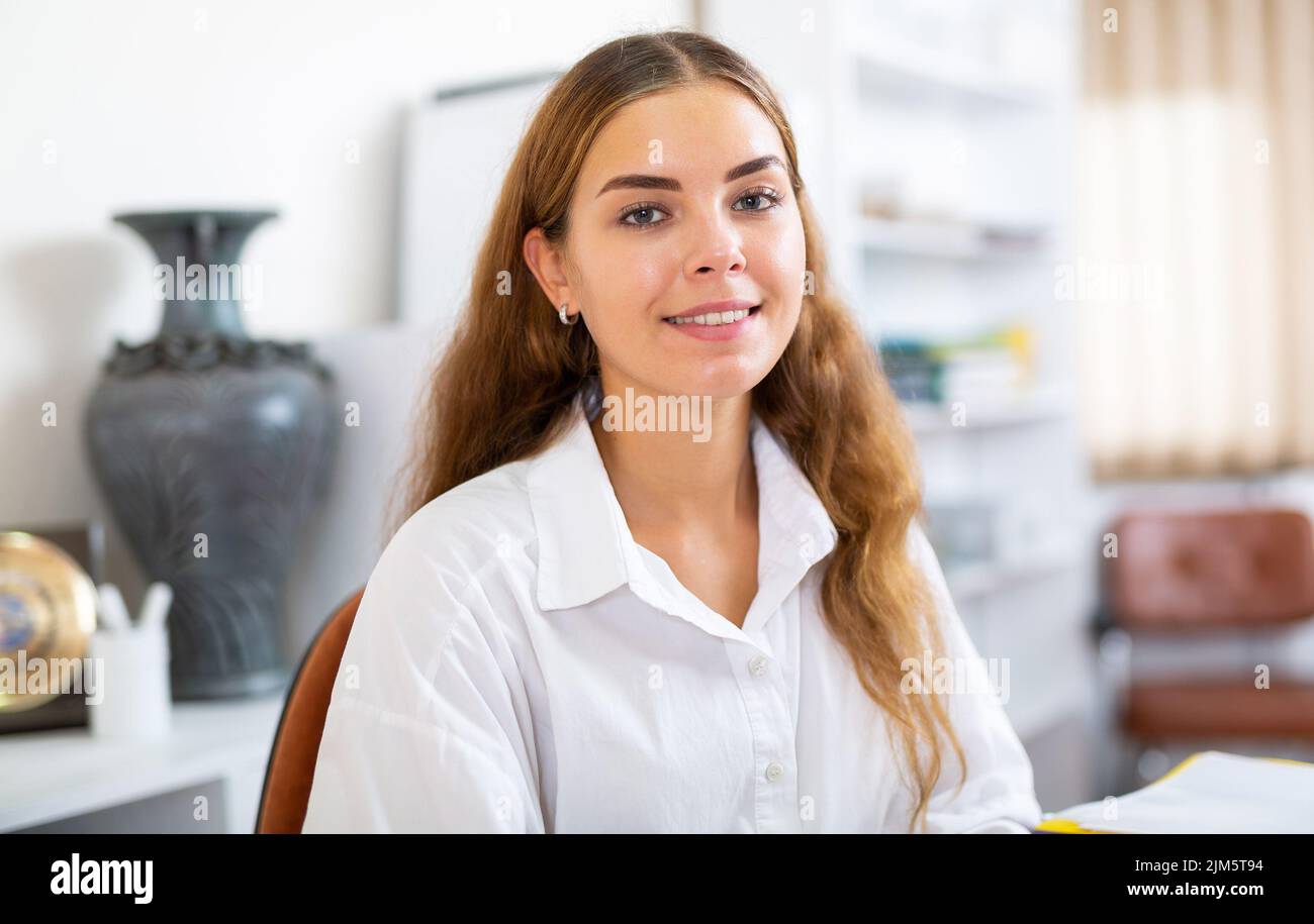 Positiva giovane donna dai capelli castani in blusa bianca in ufficio Foto Stock