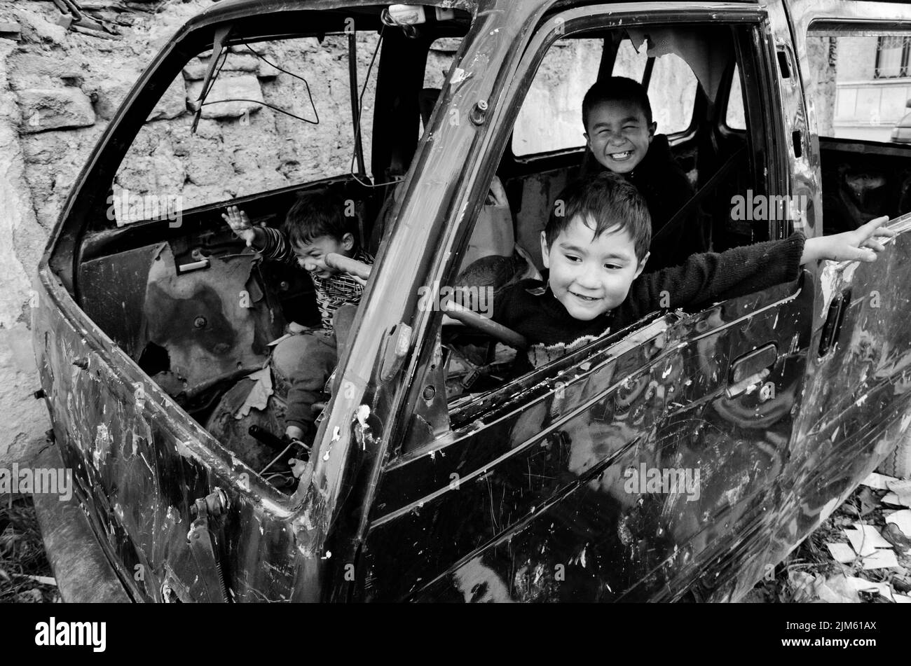 Un'immagine in scala di grigi di un gruppo di bambini che giocano all'interno di una vecchia auto bruciata a Istanbul, in Turchia Foto Stock