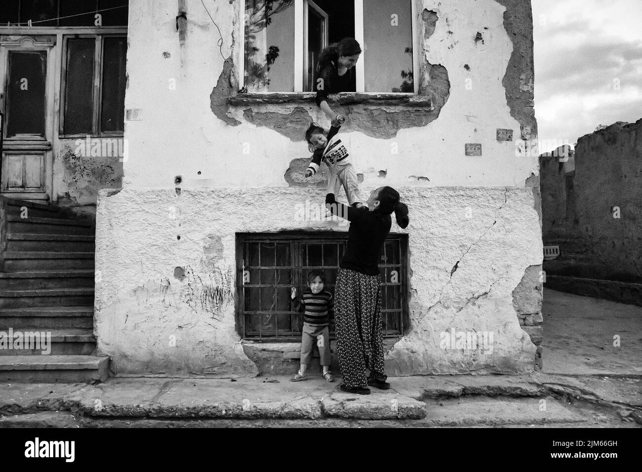 Un colpo in scala di grigi di donne con i loro bambini in un vecchio edificio in una strada in Turchia Foto Stock