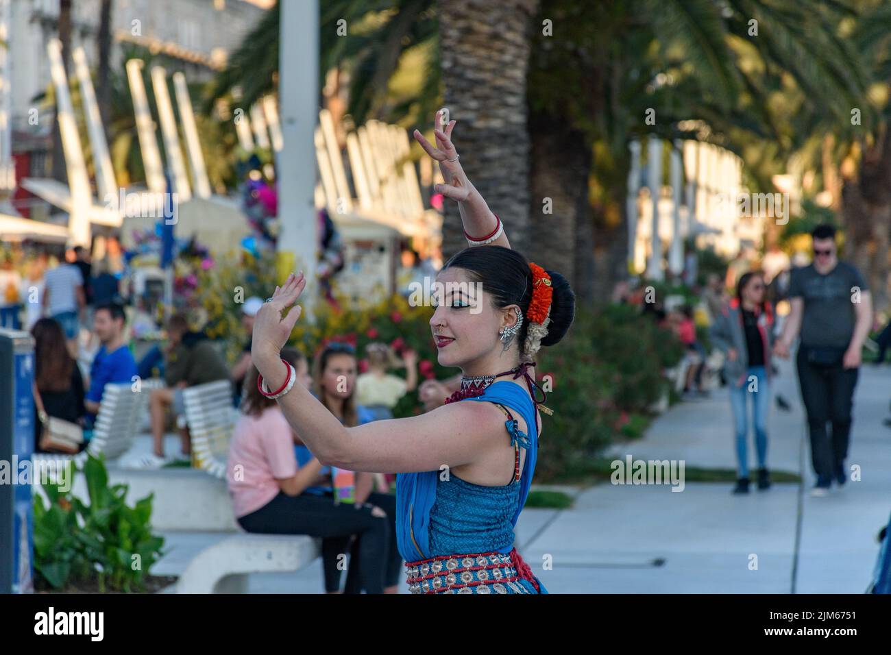 Un'artista di strada femminile esegue danza asiatica tradizionale con gesti a mano in luce del giorno con alberi verdi e persone sullo sfondo a Spalato, Croazia Foto Stock