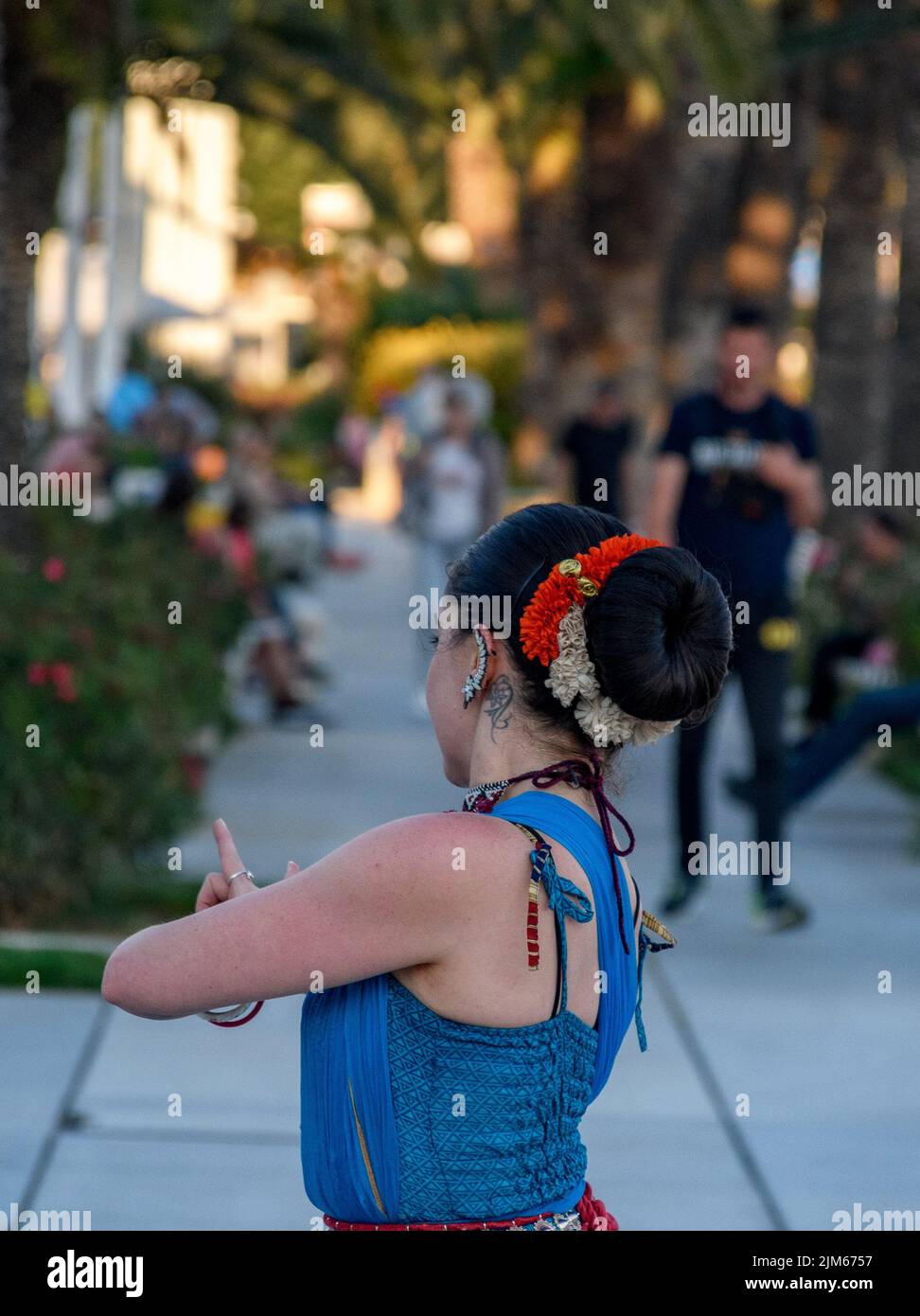 Un'artista di strada femminile esegue danza asiatica tradizionale con gesti a mano in luce del giorno con alberi verdi e persone sullo sfondo a Spalato, Croazia Foto Stock