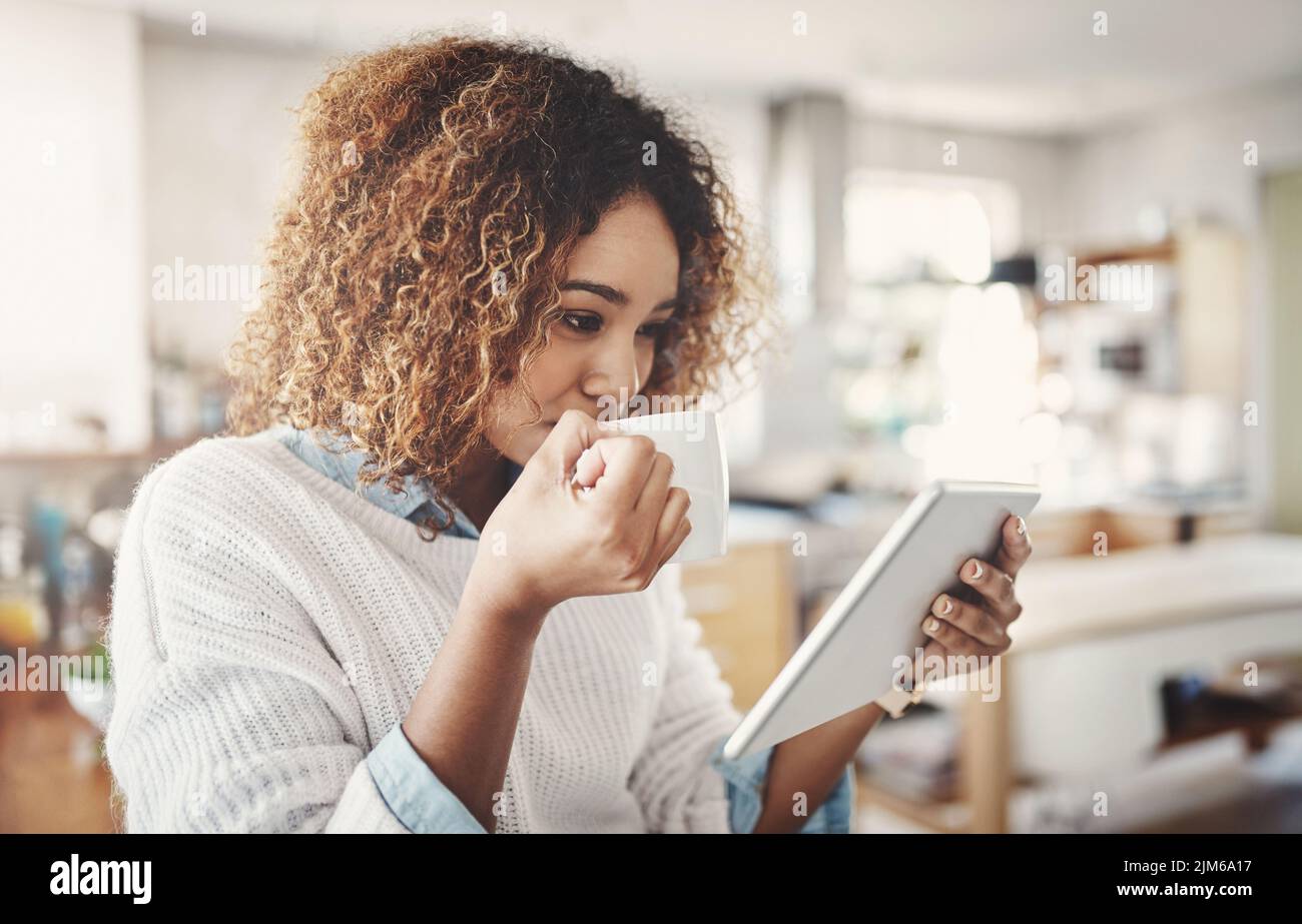 Donna rilassata, felice e spensierata che beve caffè e legge i social media su un tablet a casa. Godetevi una pausa rilassante in una tranquilla mattina o. Foto Stock