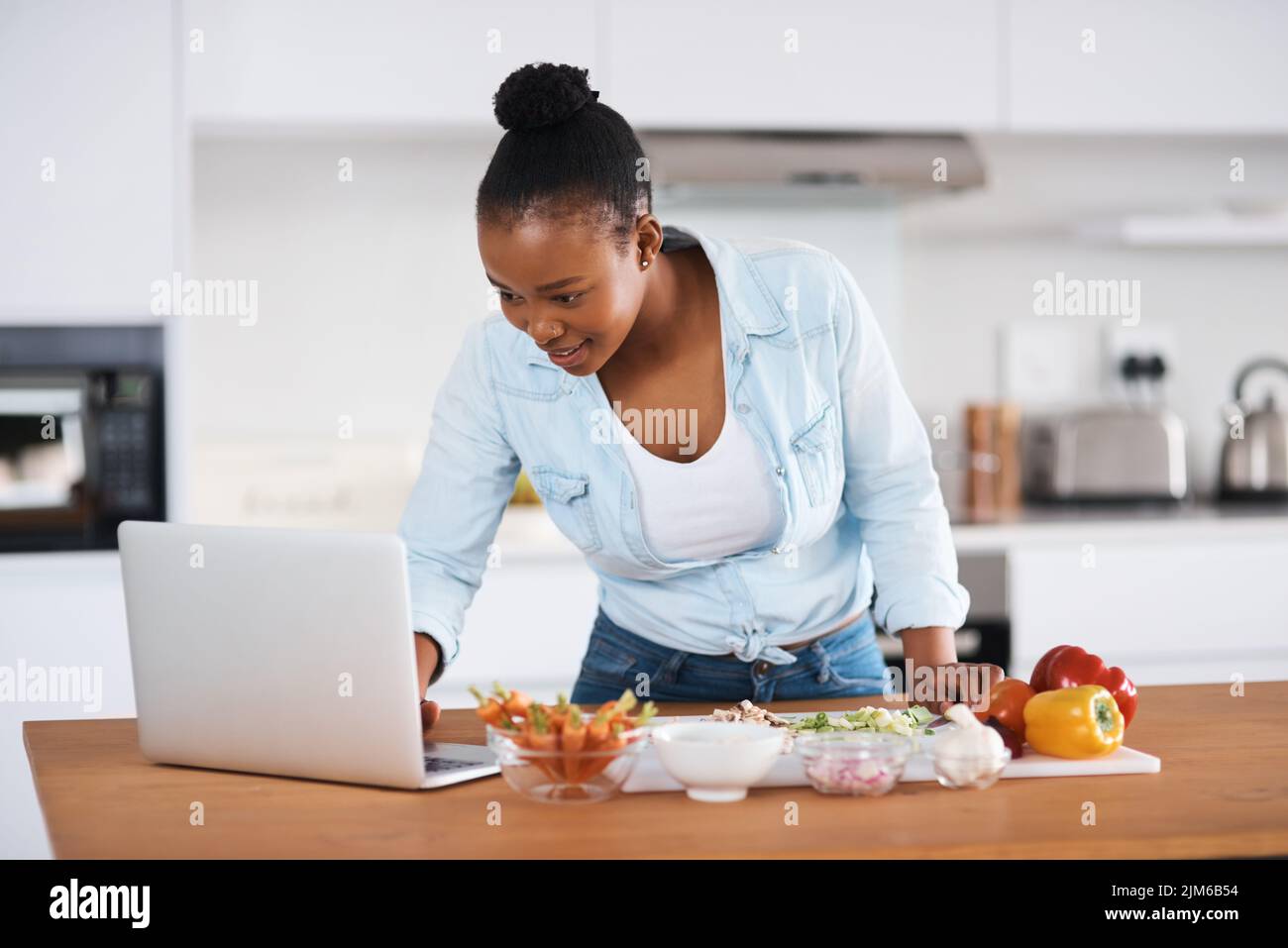 Im Sure Ill trova una ricetta facile online. Una giovane donna che usa un computer portatile mentre taglia le verdure a casa. Foto Stock