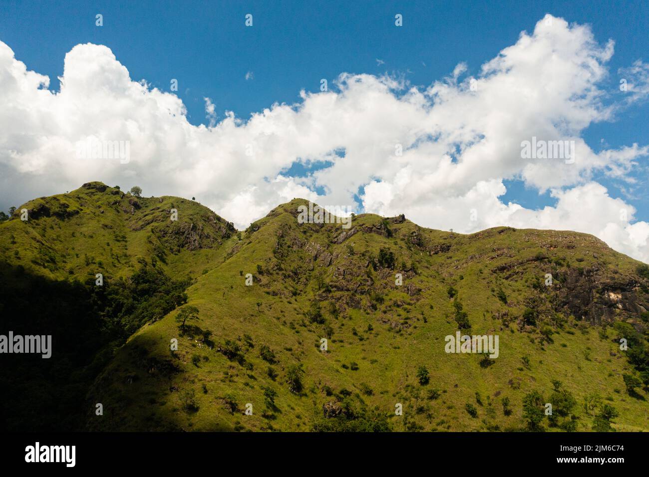 Veduta aerea dei pendii di montagna con erba verde e foresta contro il cielo blu e le nuvole. Paesaggio di montagna in Sri Lanka. Foto Stock