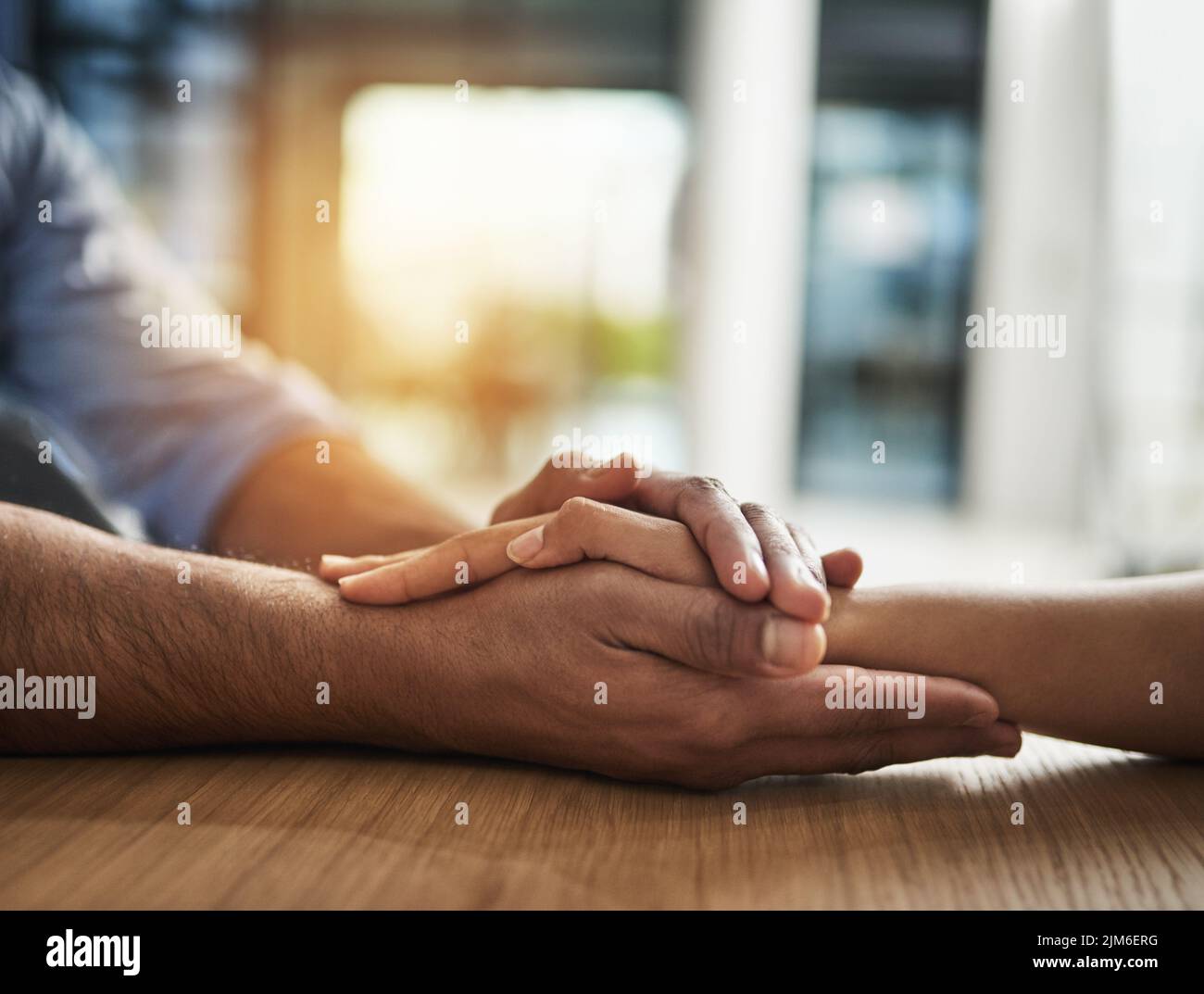 Gentilezza, sostegno e fiducia tra due persone che tengono le mani mentre si siedono a un tavolo insieme. Primo piano di due persone che parlano con tempo difficile o. Foto Stock