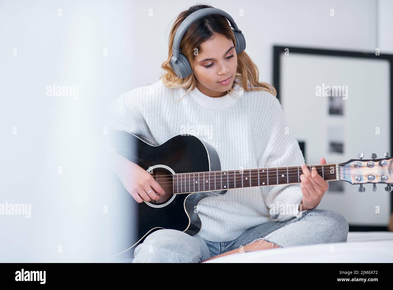 Lascia che la tua passione diventi il tuo scopo. Una giovane donna che indossa le cuffie mentre suona la chitarra a casa. Foto Stock