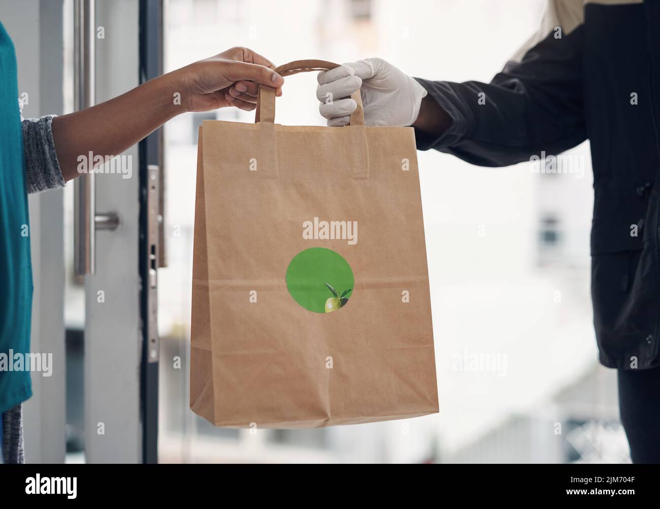 Risparmiatevi il rischio di mangiare fuori. Un uomo irriconoscibile che indossa guanti mentre consegnate il takeout a un cliente a casa. Foto Stock