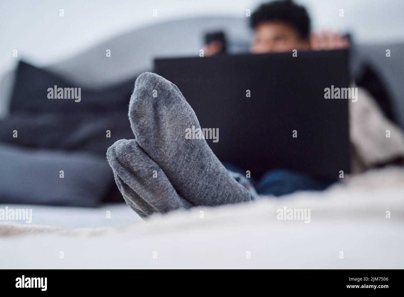 Non puoi farlo in ufficio: Un giovane che usa un computer portatile sul letto di casa. Foto Stock