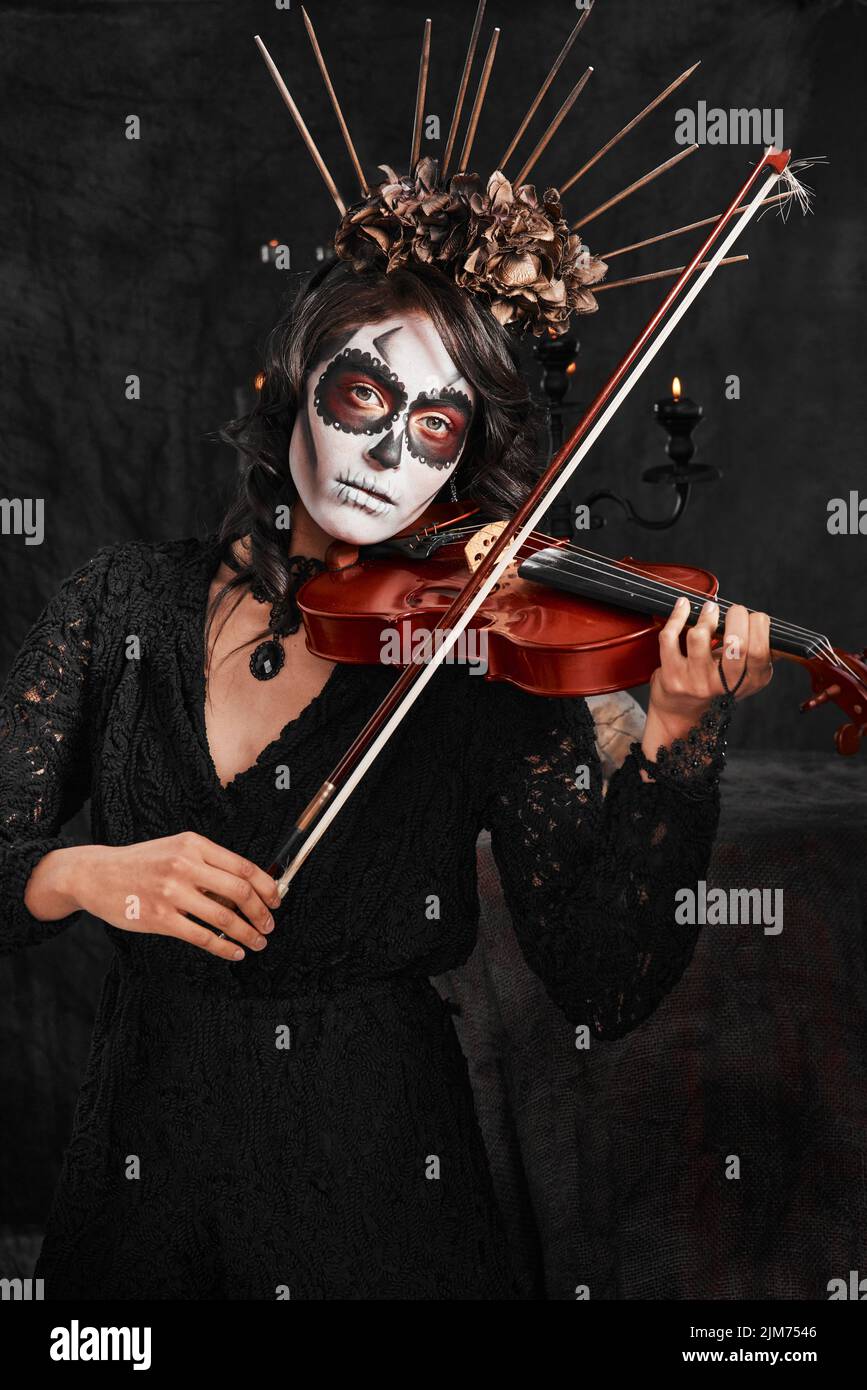 Halloween musica d'umore. Ritratto corto di una giovane donna attraente vestito con il suo costume messicano di Halloween che suona un violino. Foto Stock